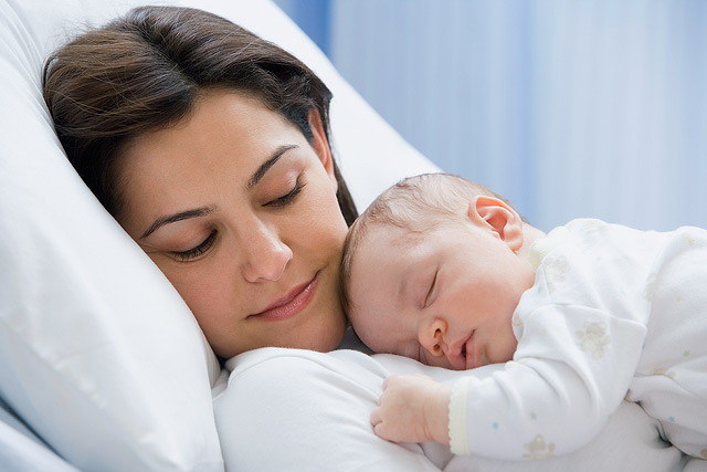 Una madre acostada con su bebé recién nacido en su cama de hospital